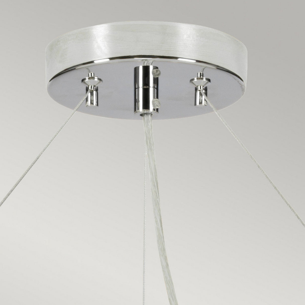 A close-up of the Pearce 34" Pendant Light - Polished Chrome Ivory Shade highlights its sleek design, featuring a polished chrome finish with a round, metallic base. Three wires extend symmetrically downward, making it an ideal fit for modern interiors. This fixture is mounted on a smooth, light-colored ceiling.