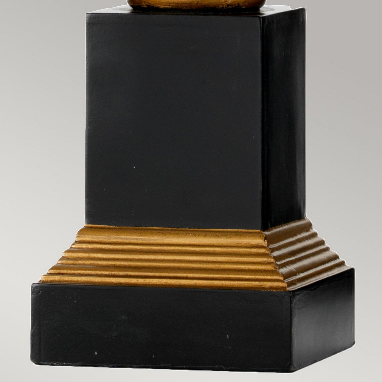 The Peronne Table Lamp with Tall Empire Shade in black and gold mimics a sophisticated design with its tiered golden base. The sleek, geometric structure showcases sharp edges and contrasting hues, set against a plain light gray background.