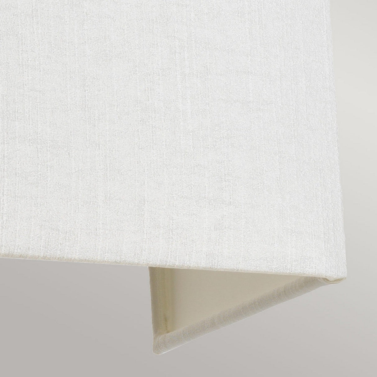 The Riley Large Rectangular Wall Light in aged brass features a textured fabric lampshade with a geometric, ivory design. Its clean lines and angular, modern style are highlighted against a plain gray background.