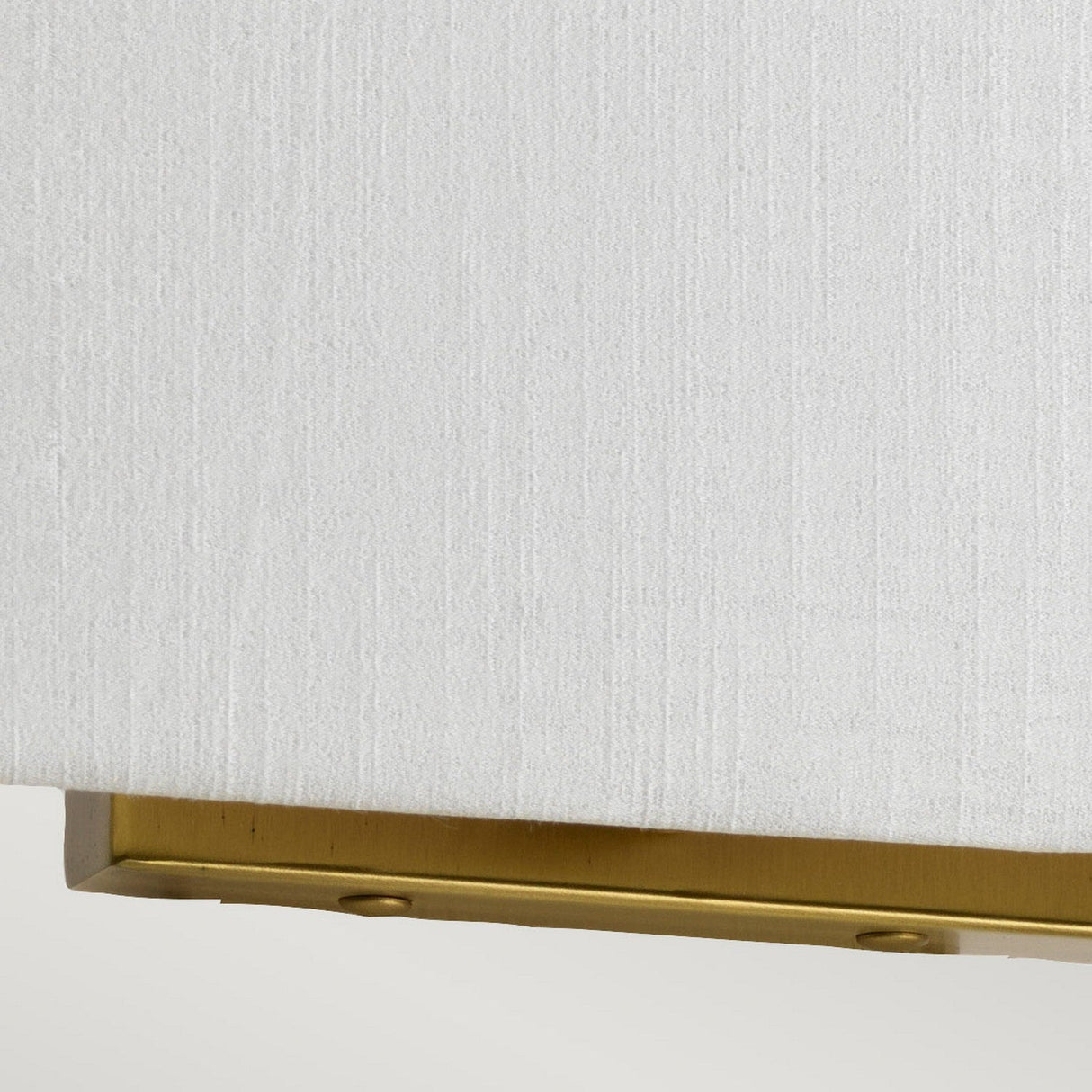 A close-up view of a white textured fabric with the Riley Medium Rectangular Wall Light in aged brass, featuring a metal strip partially visible at the bottom edge.