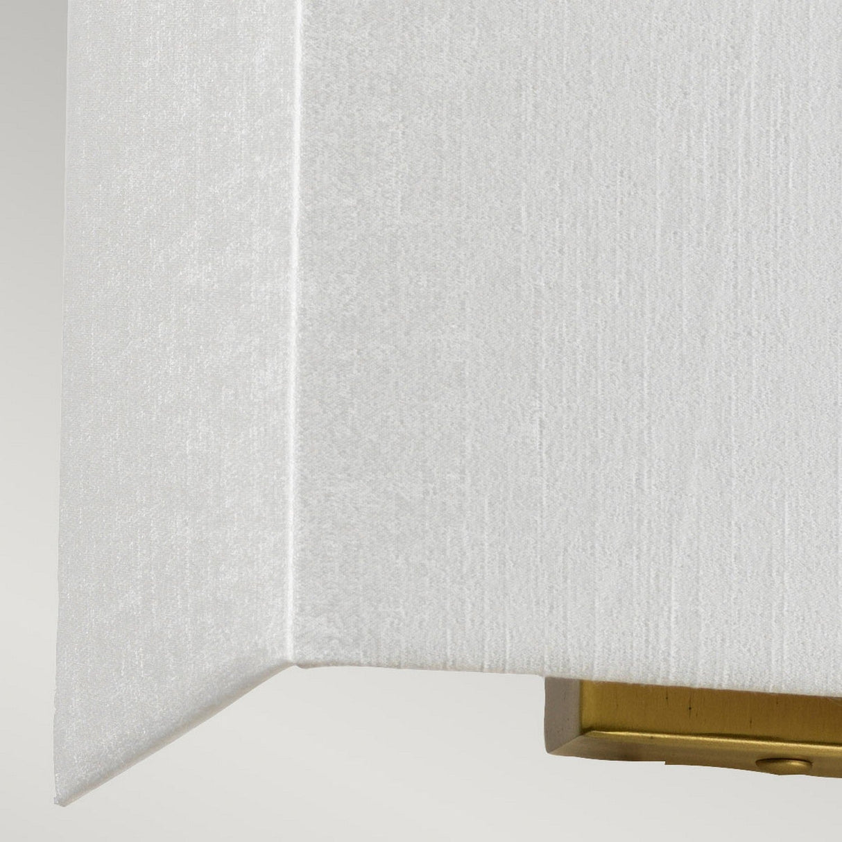 Close-up of a white textured corner with a subtle shadow, featuring the Riley Medium Rectangular Wall Light in aged brass at the bottom. The image highlights architectural details in a minimalistic style.