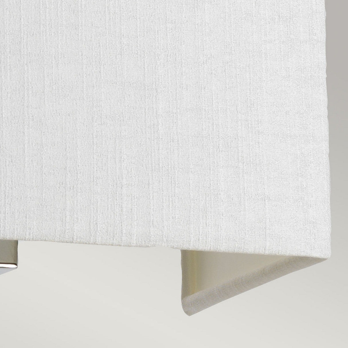 Close-up of a folded, off-white fabric with a subtle textured pattern, elegantly illuminated by ambient lighting. The smooth fabric highlights visible weave lines, enhancing its minimalist charm, akin to the sleek design of the Riley Medium Rectangular Wall Light - Polished Chrome.