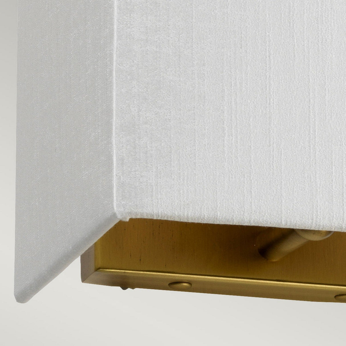 Close-up of the Riley Small Rectangular Wall Light in Aged Brass, showcasing a fabric-covered corner with a faux silk shade. The aged brass base provides a smooth metallic finish and includes a small toggle switch for convenience.
