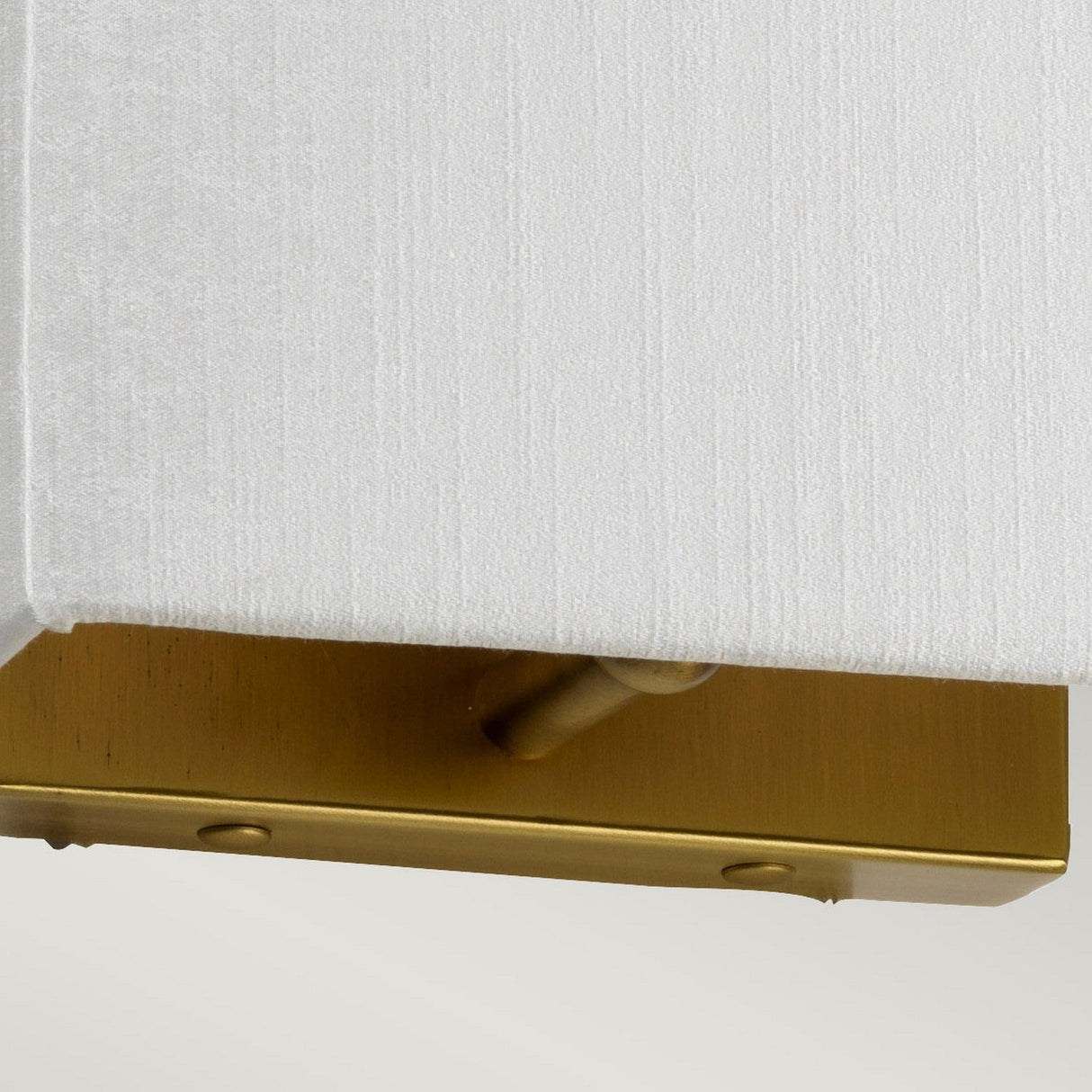 Close-up of the Riley Small Rectangular Wall Light - Aged Brass, showcasing a faux silk shade and a sophisticated aged brass metallic base. The elegantly crafted base is highlighted by a central small, round toggle switch.