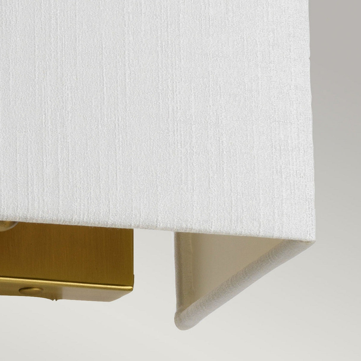 A detailed view of a faux silk shade paired with an aged brass fixture showcases the texture and precise alignment of the lampshade against a minimalist gray backdrop, highlighting the sophistication of the Riley Small Rectangular Wall Light - Aged Brass.