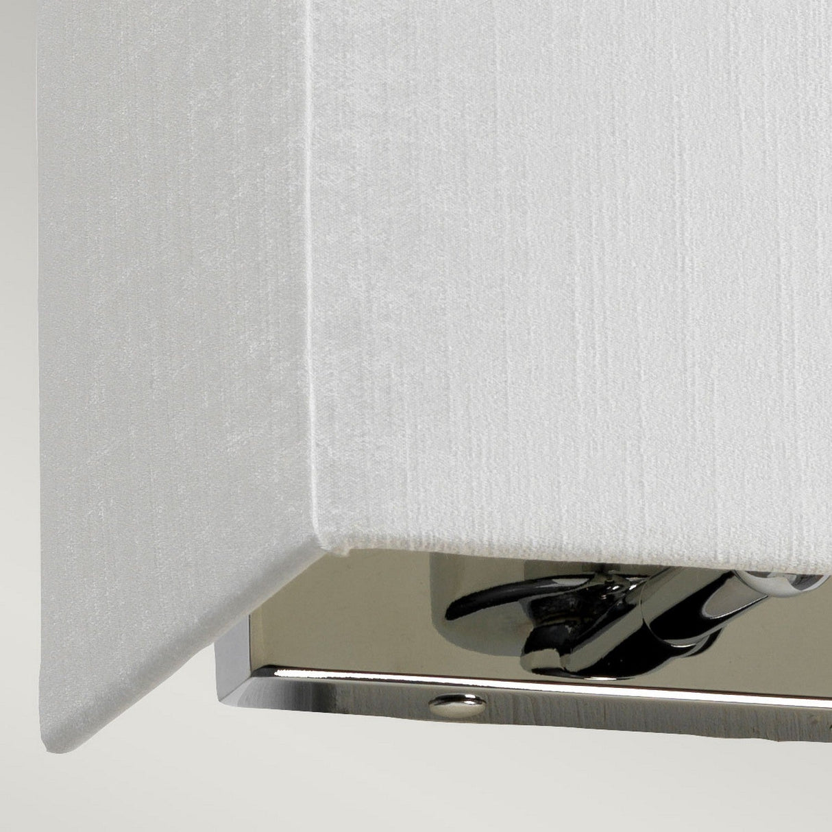 A close-up of the Riley Small Rectangular Wall Light - Polished Chrome showcases contemporary lighting excellence, featuring a textured white shade and polished chrome accents. Its geometric design offers clean lines and a sleek, polished base, adding an elegant touch to any modern space.