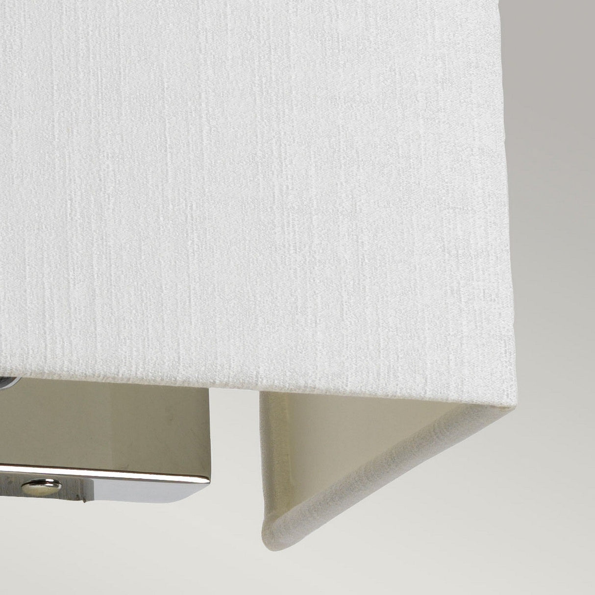 The Riley Small Rectangular Wall Light, featuring a white fabric lampshade with a textured surface, offers a glimpse of its polished chrome fixture beneath. This contemporary lighting design elegantly contrasts against the light gray background.