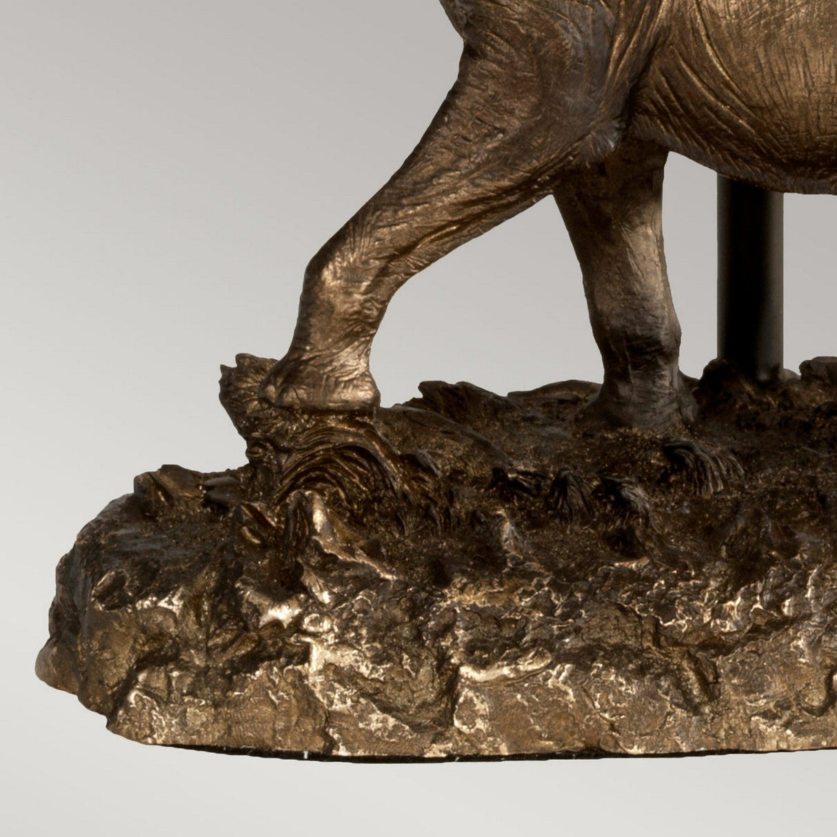 Close-up of the Sabi Table Lamp featuring an oval shade, designed with a bronze patina finish on its base that mirrors the muscular detailing and realistic texture of an animal leg, standing on a surface reminiscent of rocky terrain.