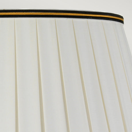 Close-up of the top section of a Sashi Table Lamp with Tall Empire Shade, highlighting its green pleated fabric with oriental craftsmanship. A gold and brown band trims the top edge, enhancing its elegance. The ambient light casts a gentle glow against the plain, light gray background.