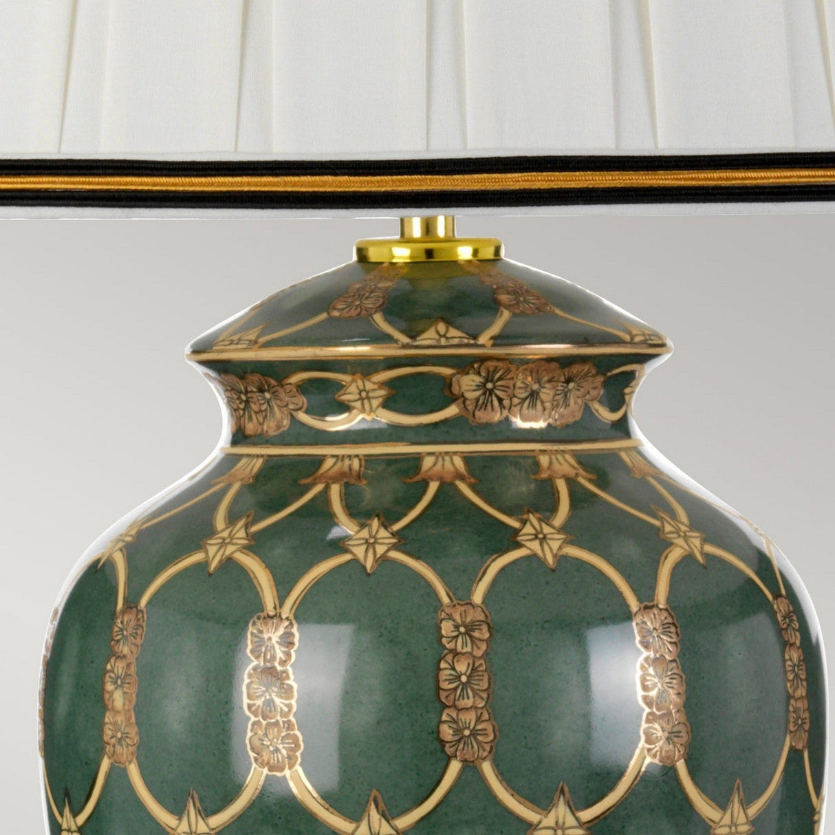 Close-up of the Sashi Table Lamp With Tall Empire Shade - Green With Gold & Brown, a masterpiece of oriental craftsmanship. The intricate gold floral patterns adorn its ornate green ceramic base, topped with a pleated white lampshade featuring black and gold trim, casting warm ambient light.