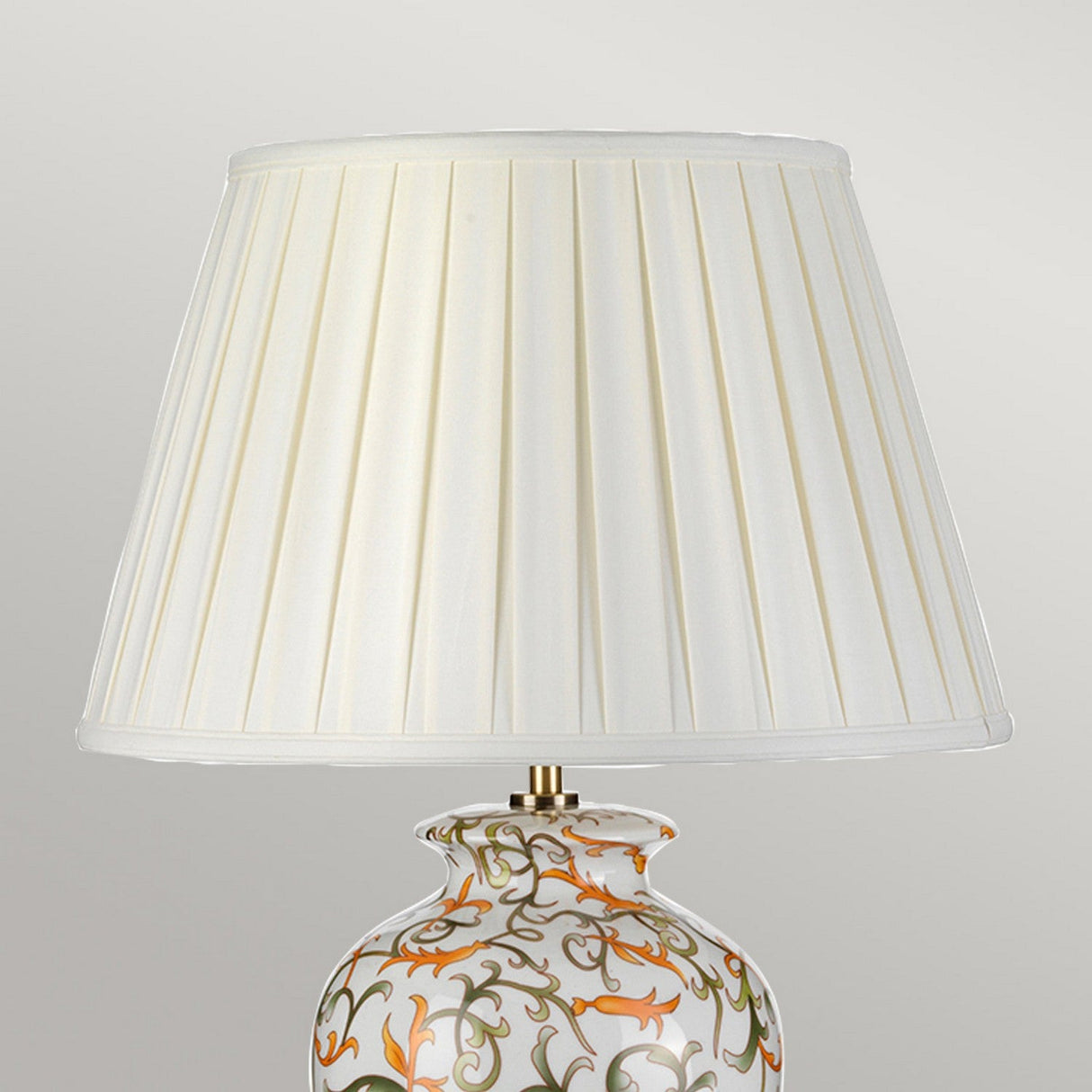 The Soling Table Lamp - Cream With Orange & Green captivates with its oriental craftsmanship, featuring a ceramic base embellished with an intricate orange and green floral design, and completed by a white pleated lampshade.