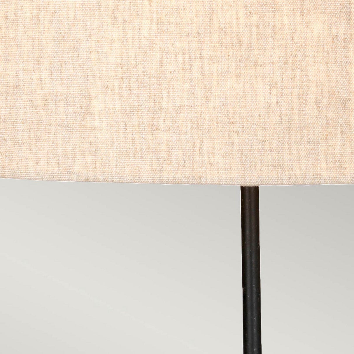 Close-up of the Spirit Table Lamp With Oval Shade - Bronze Patina, showcasing a neutral-colored fabric lampshade with a subtle woven texture atop a slender, black metal lamp stand with a bronzed finish, set against a light gray background. Ideal for infusing elegance into any space for both equestrian enthusiasts and design lovers.