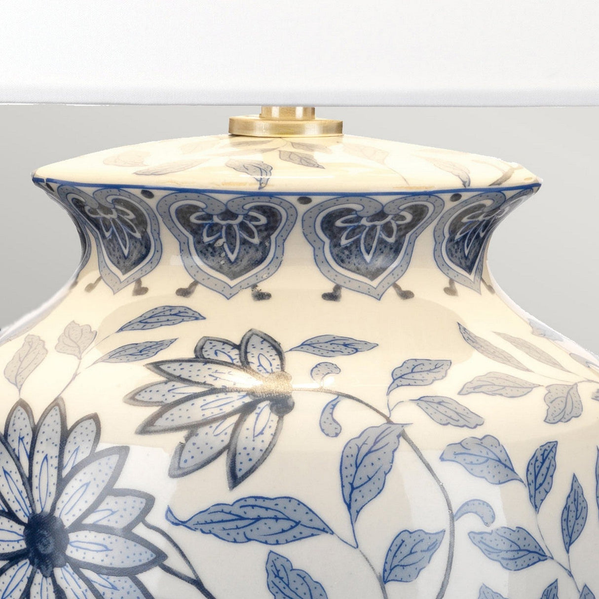 The Ying 1 Light Table Lamp - Blue & White features a close-up view of its ceramic base, adorned with intricate blue floral and leaf patterns on a cream background. Evoking classic Chinese designs, the detailed flowers and stylized leaves highlight the lamp's elegant shape, making it an ideal choice for ambient lighting in any room.