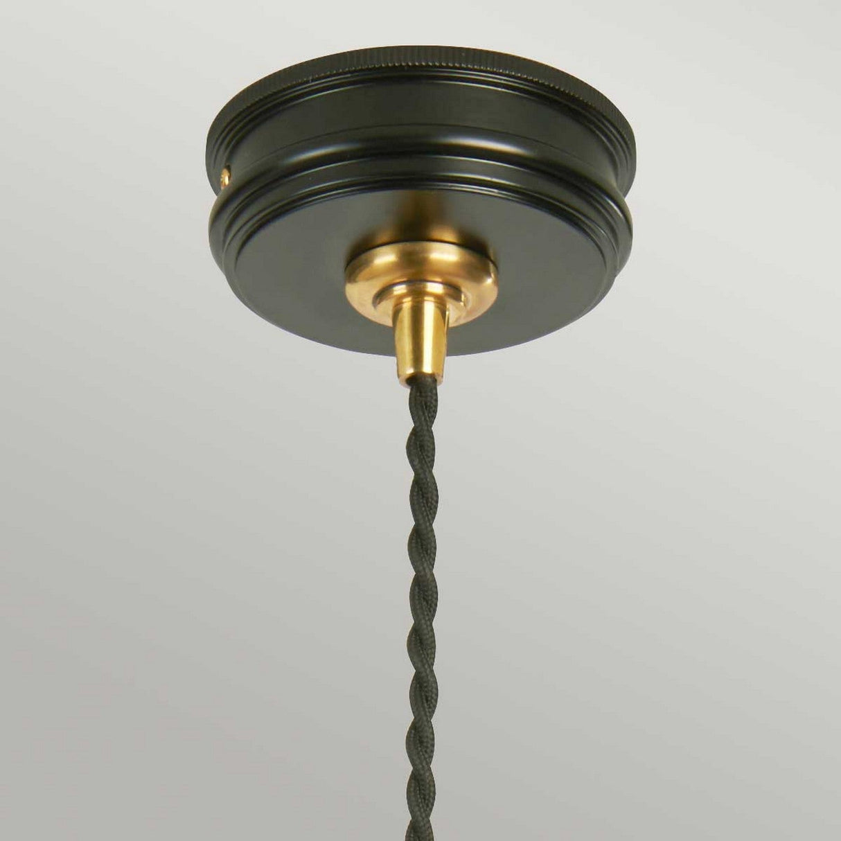 The Douille 1 Light Pendant in Black & Polished Brass is shown in a close-up view, featuring a round black canopy and a polished brass lamp holder with a twisted black cord hanging down. This fixture is set against a plain white ceiling, creating a striking contrast that highlights its elegant simplicity.
