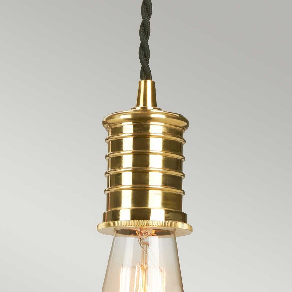 Close-up of the Douille 1 Light Pendant in an industrial style, showcasing a polished brass lamp holder and a vintage-style LED filament bulb. The pendant hangs elegantly from a twisted black cord against a neutral backdrop.