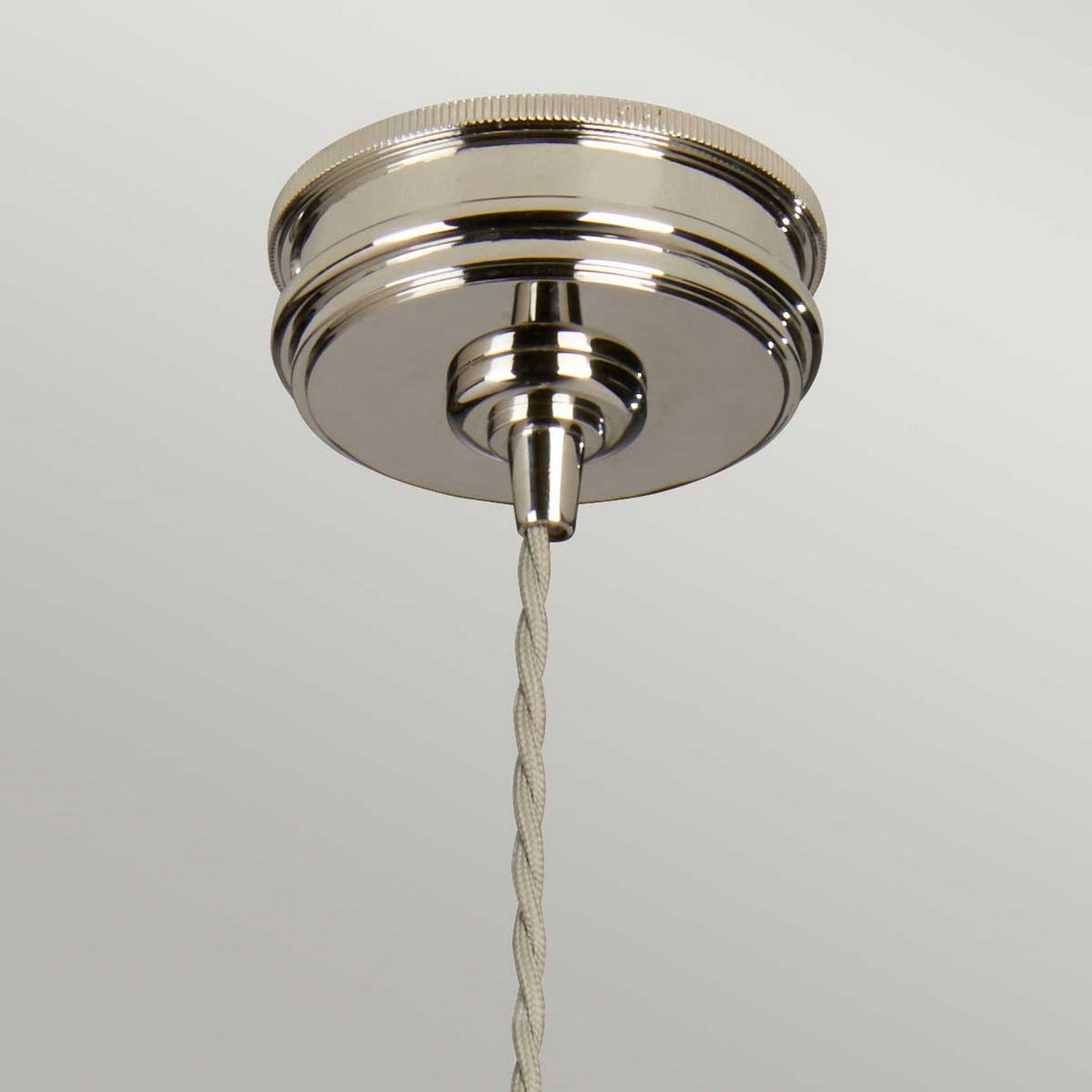 The Douille 1 Light Pendant in Polished Nickel features a twisted beige cord and a sleek, metallic surface that reflects light beautifully. It stands out against the light gray background and pairs perfectly with vintage-style LED filament bulbs, capturing the essence of an industrial pendant light.