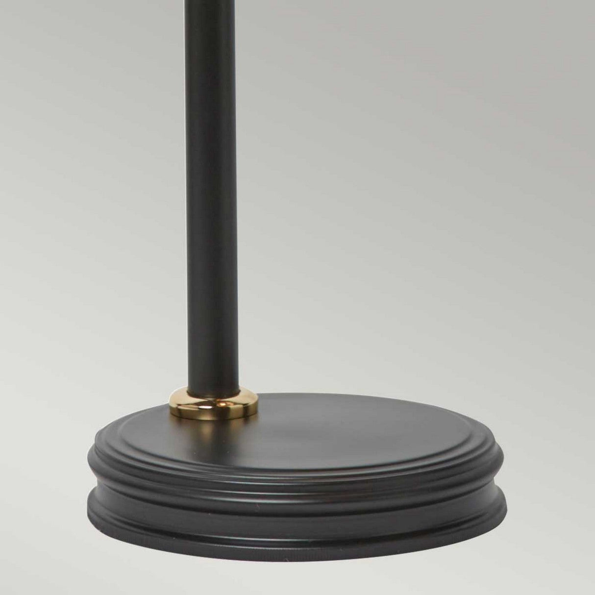 Here's a rephrased version incorporating the product data:
A detailed view of the Douille Table Lamp - Black & Polished Brass showcases its minimalist design. The sleek, black circular base is elegantly adorned with subtle ridges and includes a touch of polished brass at the junction where the pole meets the base. The plain, neutral gray background highlights its timeless elegance.