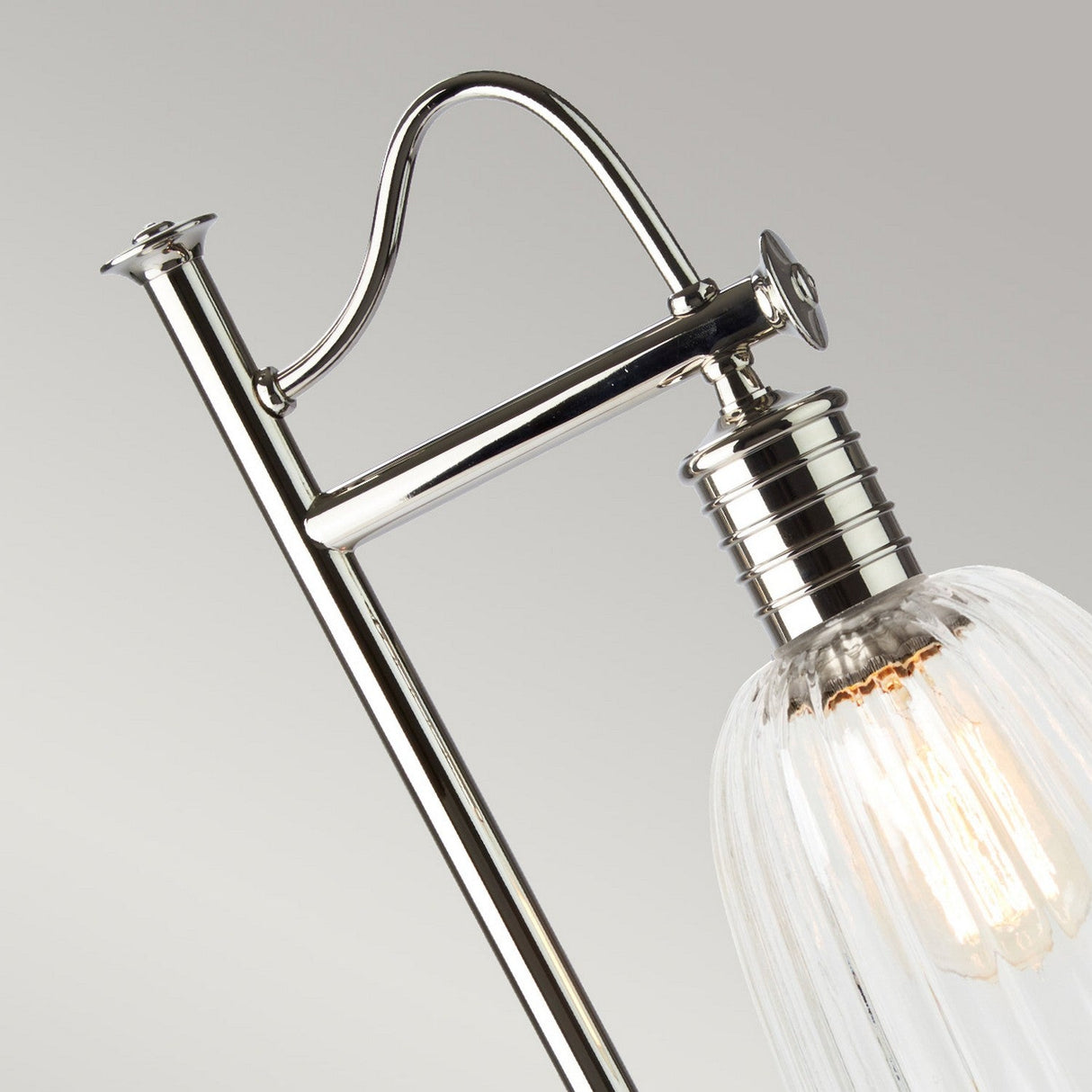 Close-up of the Douille Table Lamp in polished nickel, showcasing its sleek chrome details, ribbed glass shade, and vintage-style LED filament bulb, set against a neutral background. The lamp is elegantly designed with a curved arm that enhances its modern aesthetic.