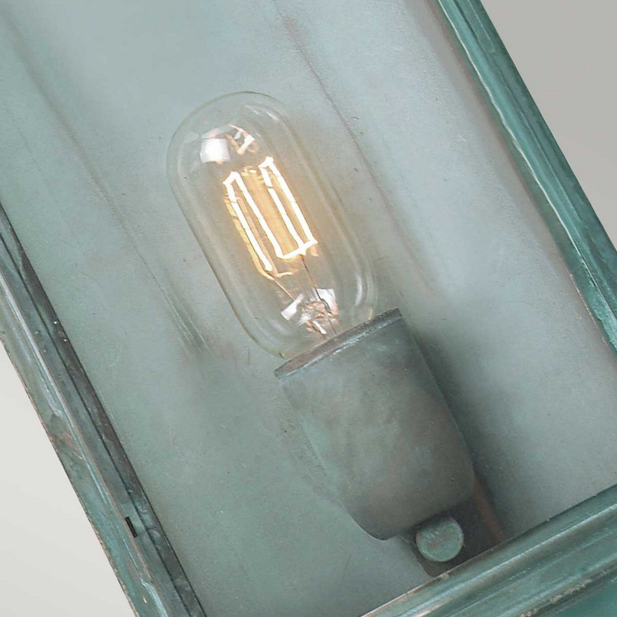 A Downing Outdoor Wall Light - Turquoise features a vintage-style bulb with visible filaments, encased in a solid brass fixture. The fixture has a slightly weathered teal patina that exudes rustic charm, enhancing the industrial design.