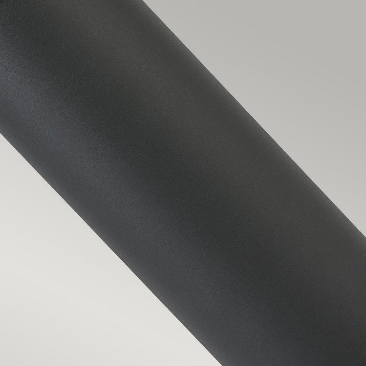 A close-up image of a graphite Egersund LED Short Bollard positioned diagonally on a gradient light gray background. The minimalist design highlights its energy-efficient illumination, providing a sleek aesthetic ideal for outdoor lighting.