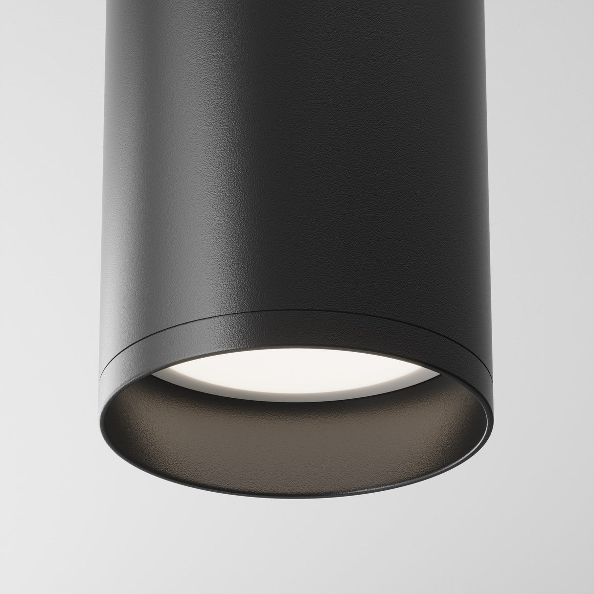 The Focus Fixed Round Surface Mounted Downlight in black, shown against a white background, is turned on and emits a soft glow. This modern lighting solution boasts a smooth matte finish and cylindrical shape.