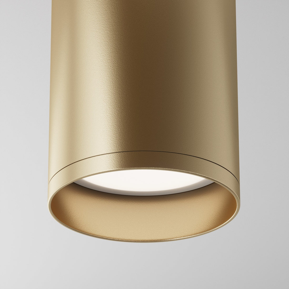 A close-up of the Focus Fixed Round Surface Mounted Downlight in matte gold reveals its modern cylindrical design with a smooth finish, highlighting a white light source at the center, exuding elegance against a plain backdrop.