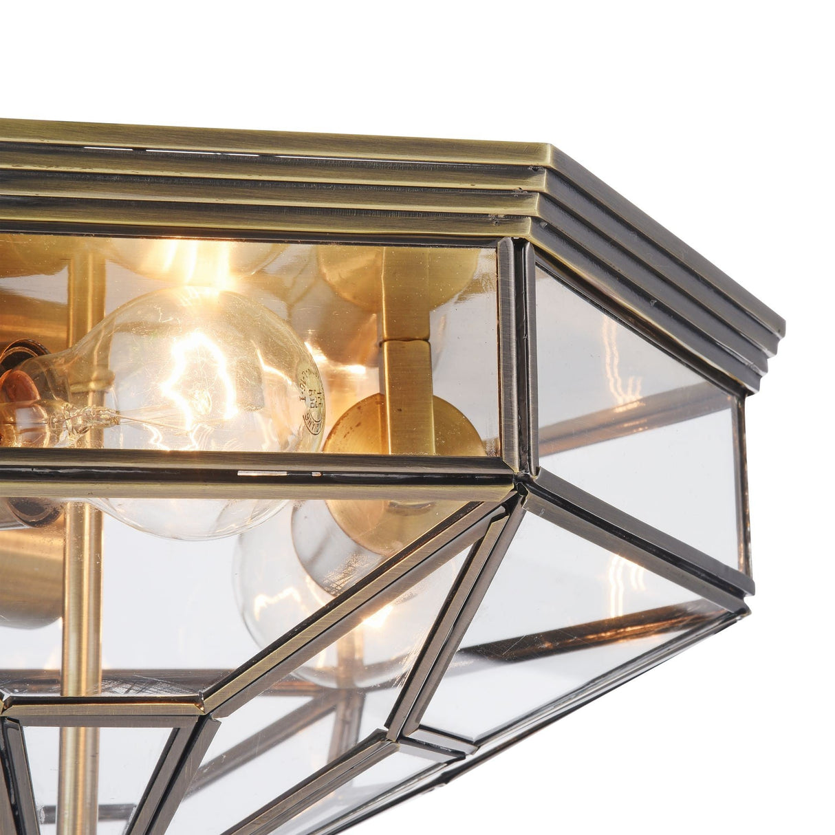 Close-up of the Zeil 3 Light Flush - Bronze featuring a geometric design with a brass frame and clear blown-glass panels. E27 bulb sockets are visible, and metallic edges form an intricate pattern, blending modern elegance with industrial flair for a striking ceiling fixture.