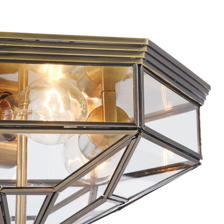 Close-up of the Zeil 3 Light Flush - Bronze featuring a geometric design with a brass frame and clear blown-glass panels. E27 bulb sockets are visible, and metallic edges form an intricate pattern, blending modern elegance with industrial flair for a striking ceiling fixture.