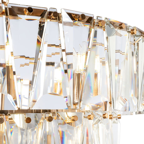Close-up of the Puntes 18 Light Chandelier - Gold, showcasing a three-tier design with multiple triangular prisms mounted on a gold frame. Light shines through, creating colorful reflections.