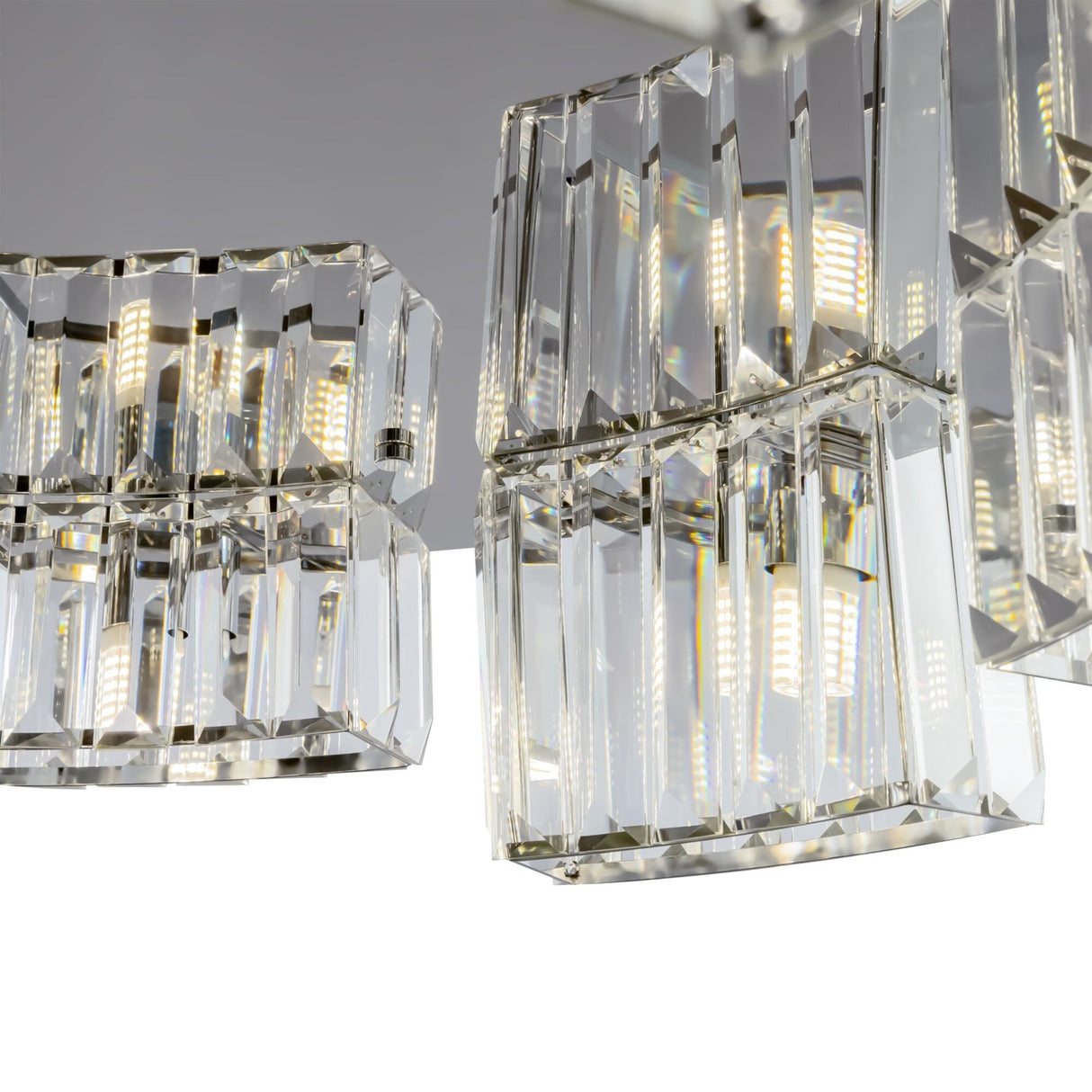 A close-up of the Colline 9 Light Suspension showcases three square crystal shades with LED lights. The chrome finish and glass pendants lend modern elegance, while the facets sparkle against a white background.