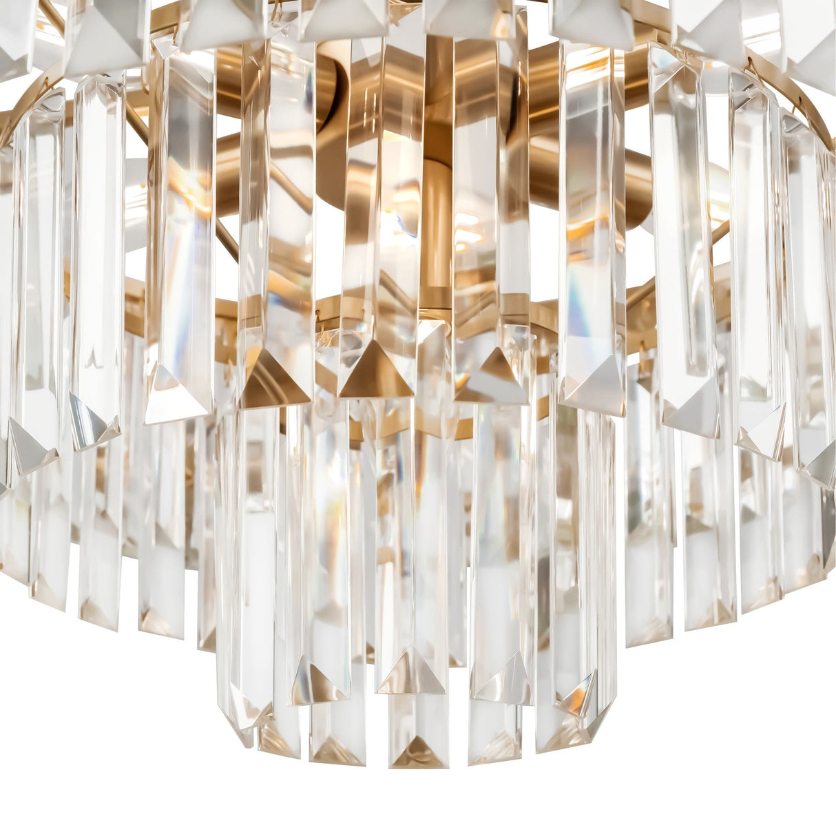 A close-up of the Revero 7 Light Chandelier - Brass highlights its vertical crystal prisms suspended from a polished brass frame, reflecting light to create a sparkling, elegant look with stunning crystal pendants.