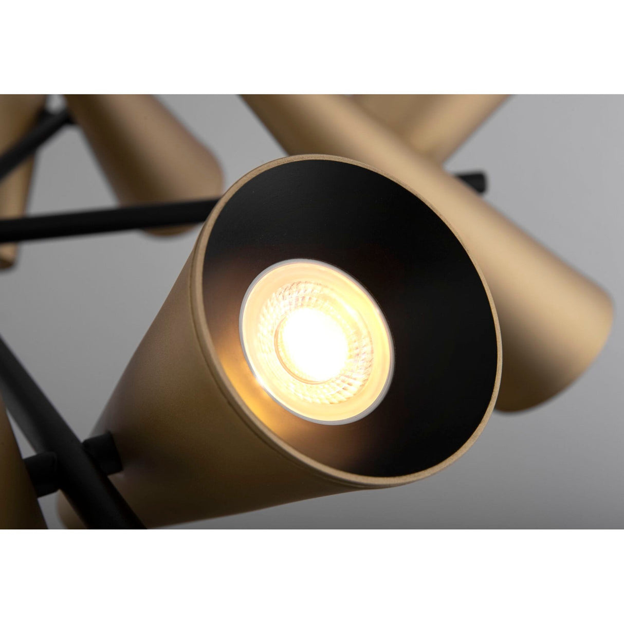 Close-up of a modern light fixture with a brass cone-shaped lampshade from the Giro 10 Light Cone Chandelier - Brass. The illuminated bulb casts a warm glow, while similar cones in the background highlight its industrial design.