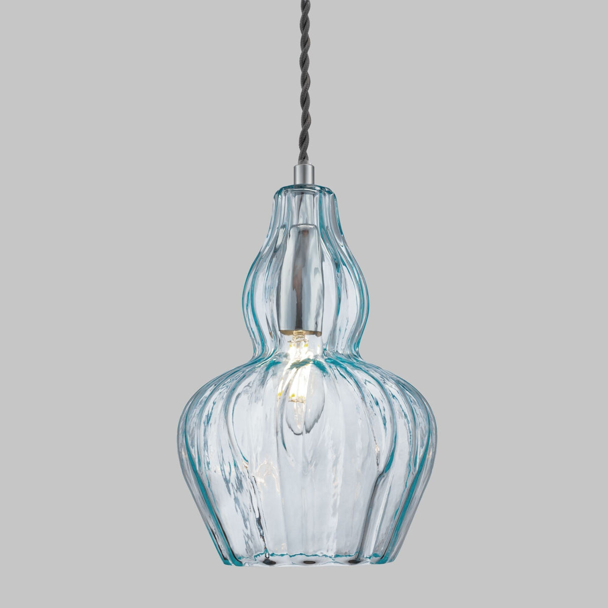 The Eustoma Pendant Light - Nickel With Light Blue Glass has a twisted black cord and intricately shaped glass shade. It features a warm glowing bulb, a sophisticated nickel finish, and modern elegance that pops against a plain gray background.