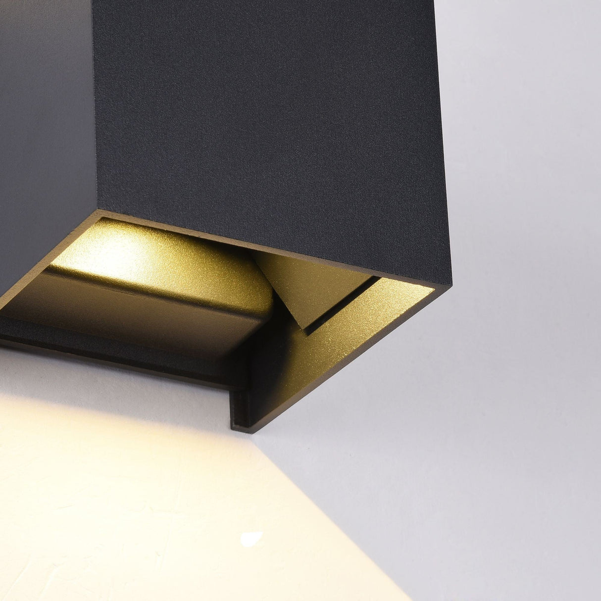 Close-up of the Fulton Outdoor LED Rectangular Wall Light in black, showcasing its modern design and smooth, corrosion-resistant aluminum. It emits a soft, warm light that casts subtle shadows on the adjacent white wall.