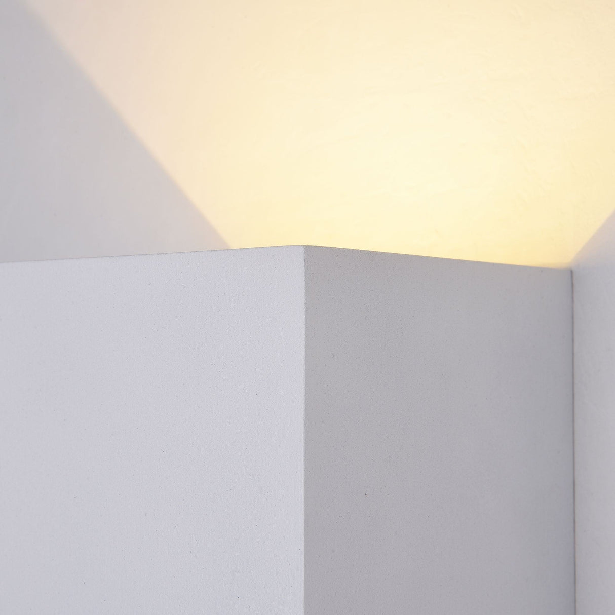The Fulton Outdoor LED Rectangular Wall Light in White features a minimalist design crafted from corrosion-resistant aluminum, emitting soft white light and casting shadows on intersecting surfaces. Its clean geometric lines and angles offer a calming, modern aesthetic.