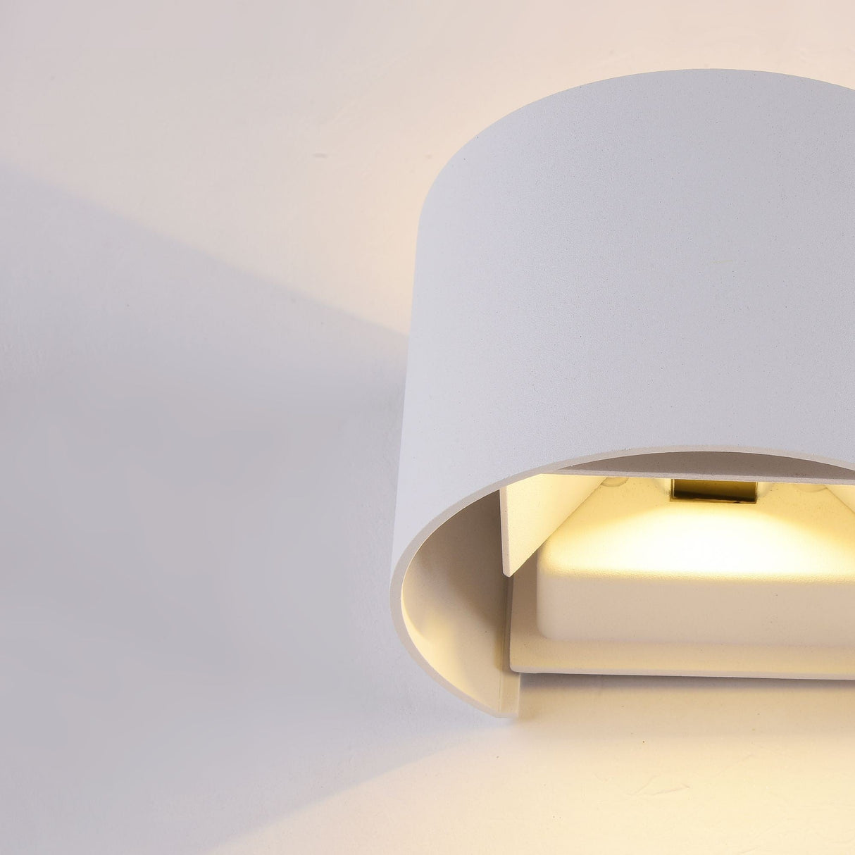 The Fulton Outdoor LED Oval Wall Light - White features a modern, curved design that emits a warm glow. Its minimalist semi-circular shape encloses an energy-efficient source, casting soft shadows. Crafted from corrosion-resistant aluminum, its durable and ideal for light-colored walls.