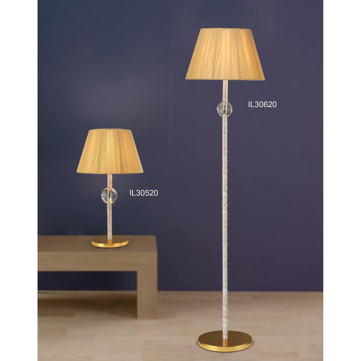 The Elena 1 Light Crystal Floor Lamp - Gold (Without Shade) (IL30620) and a matching table lamp (IL30520), both with beige pleated shades, bring luxury lighting to a modern room with a dark blue wall and light wood floor.
