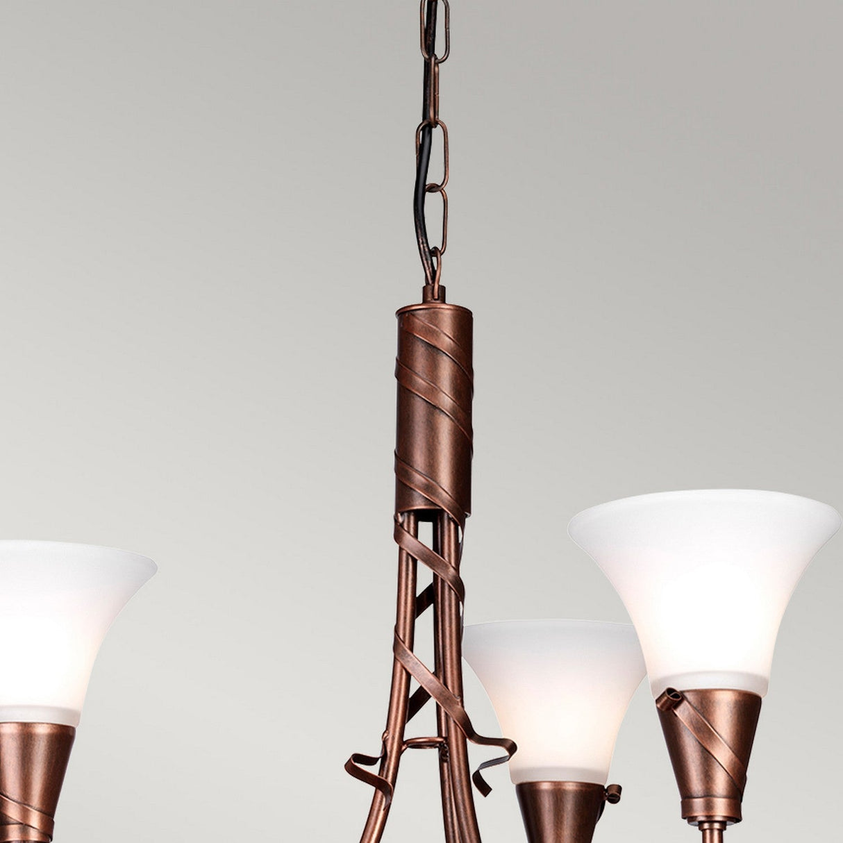 A close-up of the Emily 3 Light Chandelier in a copper patina finish showcases its intricate metalwork and three white glass shades. Ideal for vintage interiors, this design features elegant spiral details set against a neutral background.
