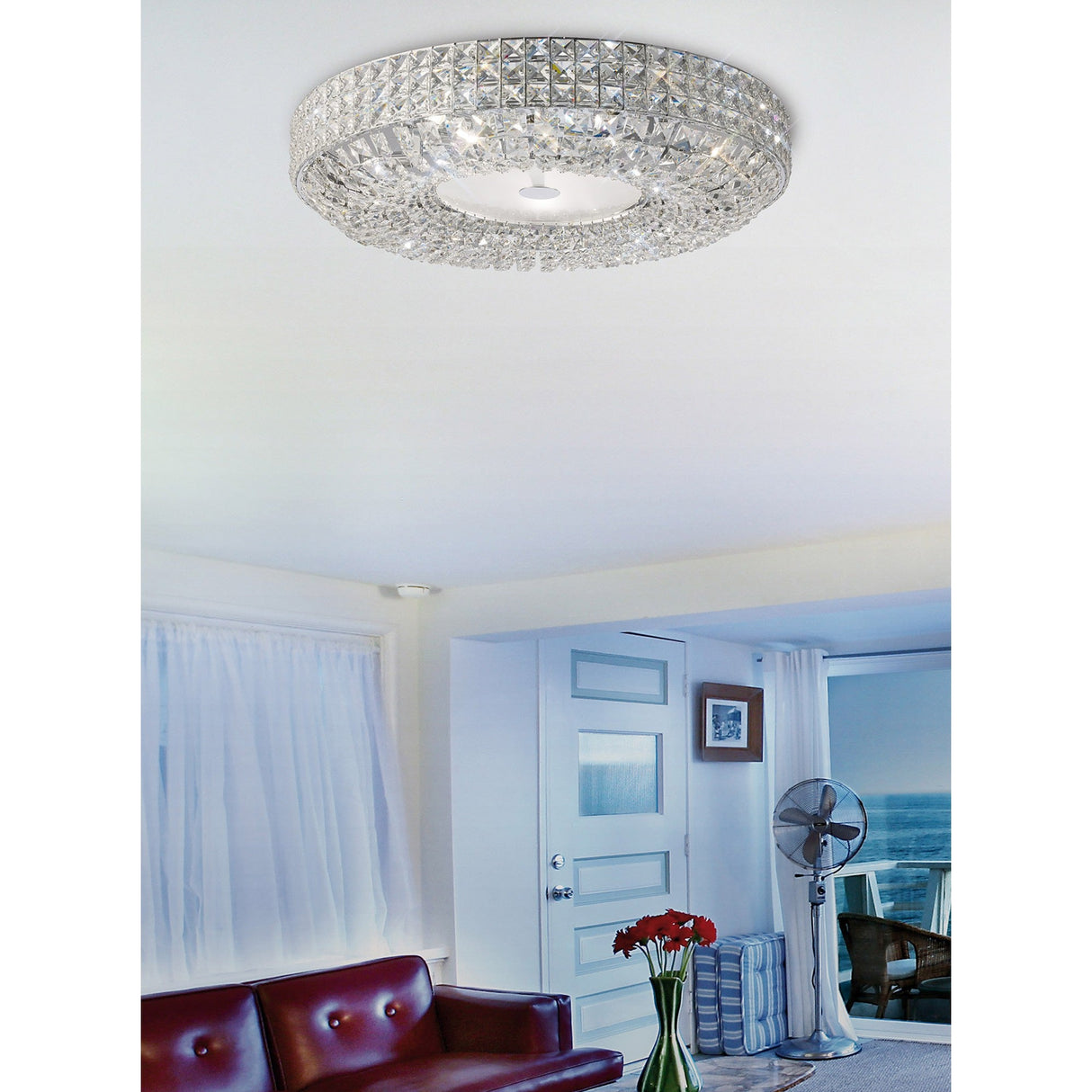 Diyas Enya 9 light crystal flush ceiling light in polished chrome, mounted on a white ceiling above a coastal living room with red sofa and sea view.