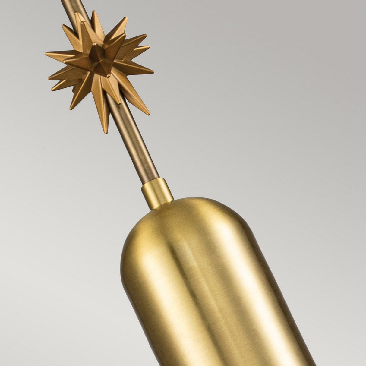 A close-up of the Etoile 1 Light Medium Pendant in an aged brass finish, showcasing its cylindrical base and decorative star-shaped accent on top, set against a plain gray background.