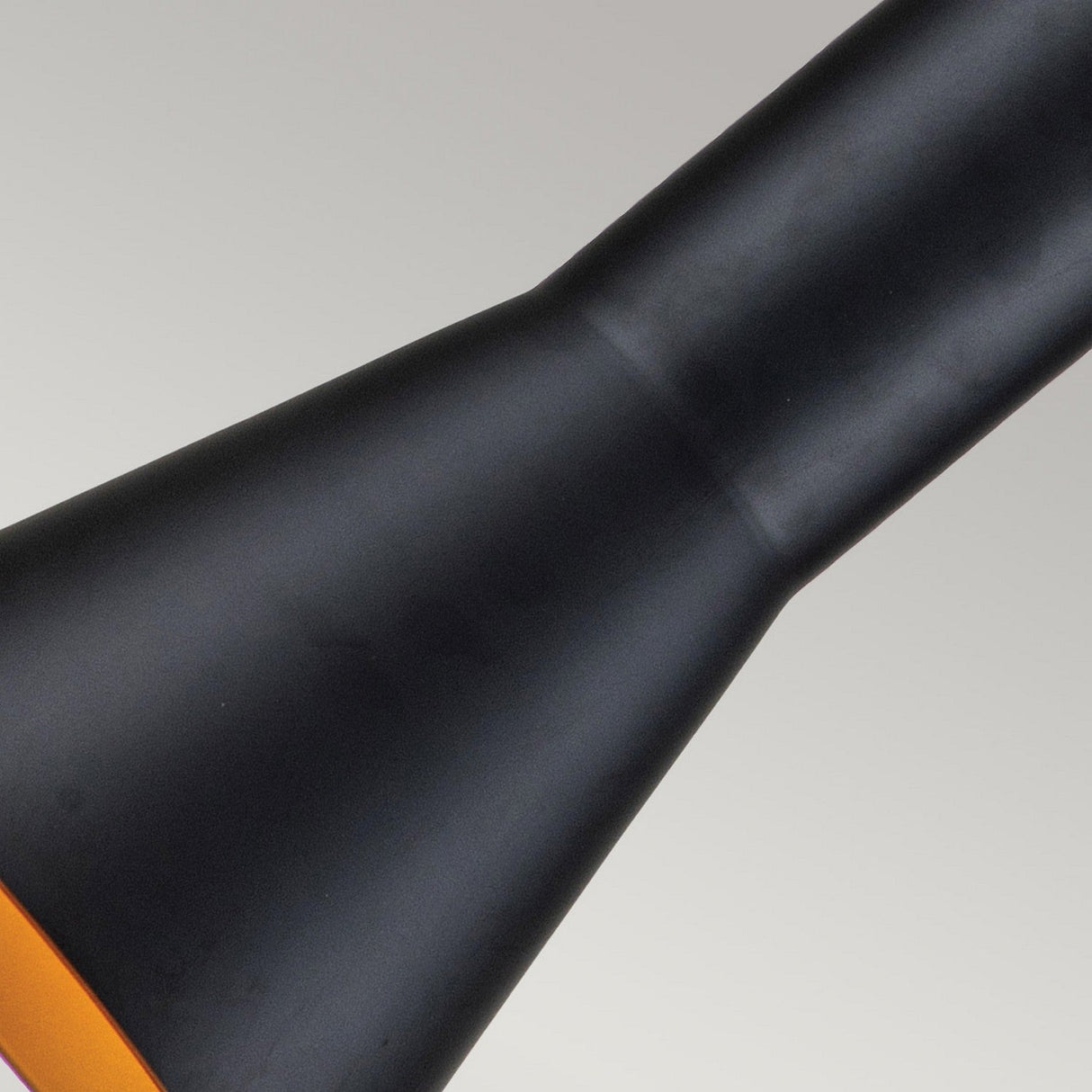 A detailed view of the Etoile 1 Light Medium Pendant in matte black reveals the star-shaped upper section of the lampshade, set against a neutral gray backdrop. The lamp interior emits a warm orange glow.