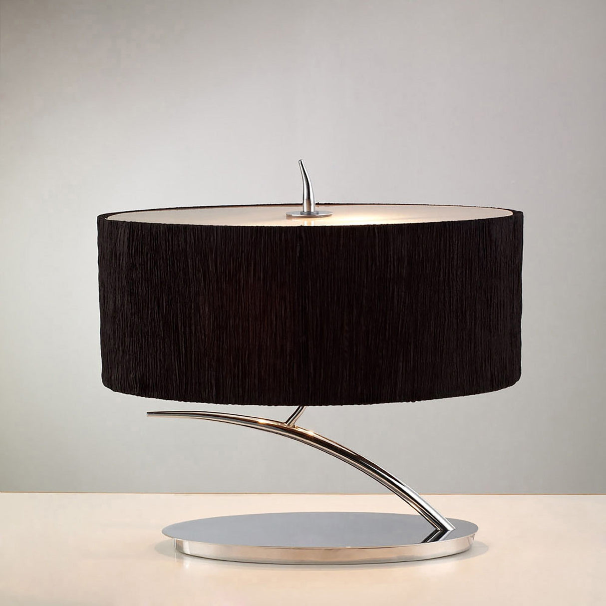 The Eve 2 Light Table Lamp features a polished chrome base and a black oval shade, displayed on a light surface with a plain gray background.