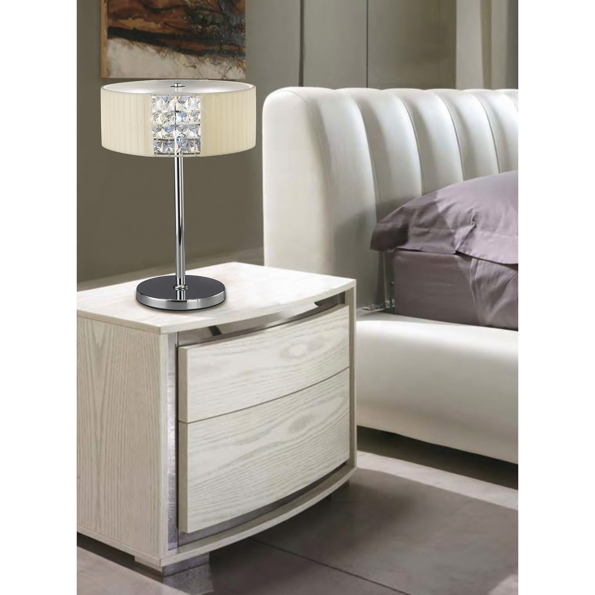 A modern bedroom features a white upholstered bed, gray bedding, and a light wood nightstand. The Evelyn 2 Light Crystal Table Lamp in chrome with a cream shade adds a touch of luxury lighting to the space.