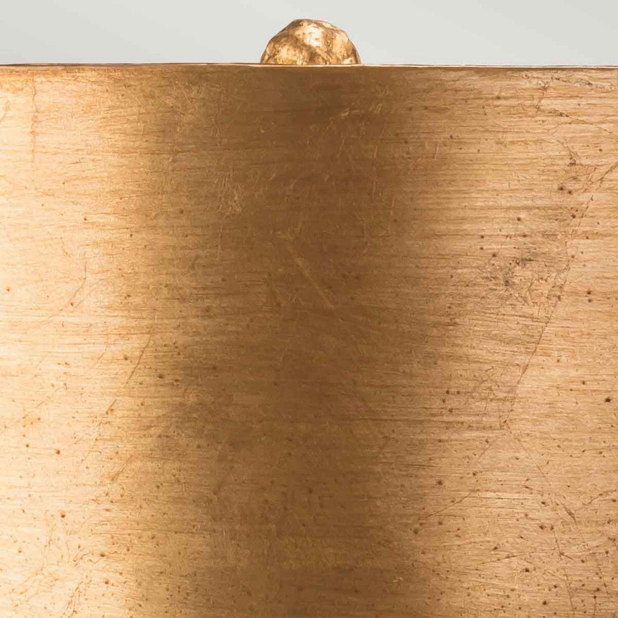 A small, spherical object rests on a flat, textured golden surface reminiscent of a Bienville 1 Light Table Lamp in Silver/Gold and Brown. The background is out of focus, highlighting the contrast between its smooth finish and the modern style texture below it.