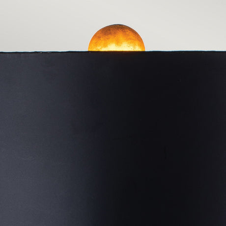 A vibrant orange sphere, reminiscent of a glowing sunset and partially visible above a dark, flat surface against a light background, evokes the warm glow of the Camilia 1 Light Table Lamp in Antique Gold & Black. It adds an elegant decorative element to any room.