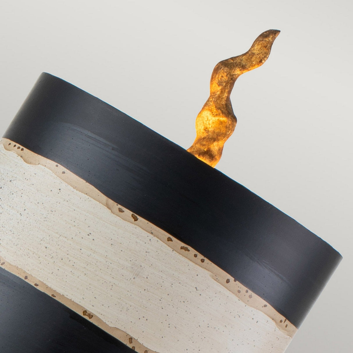 Close-up of the Dominique 1 Light Table Lamp, featuring a sleek black and cream striped design. A textured, flame-like shape extends boldly from the top, adding a dynamic touch reminiscent of modern table lamps. Hints of gold leaf accentuate its refined elegance.