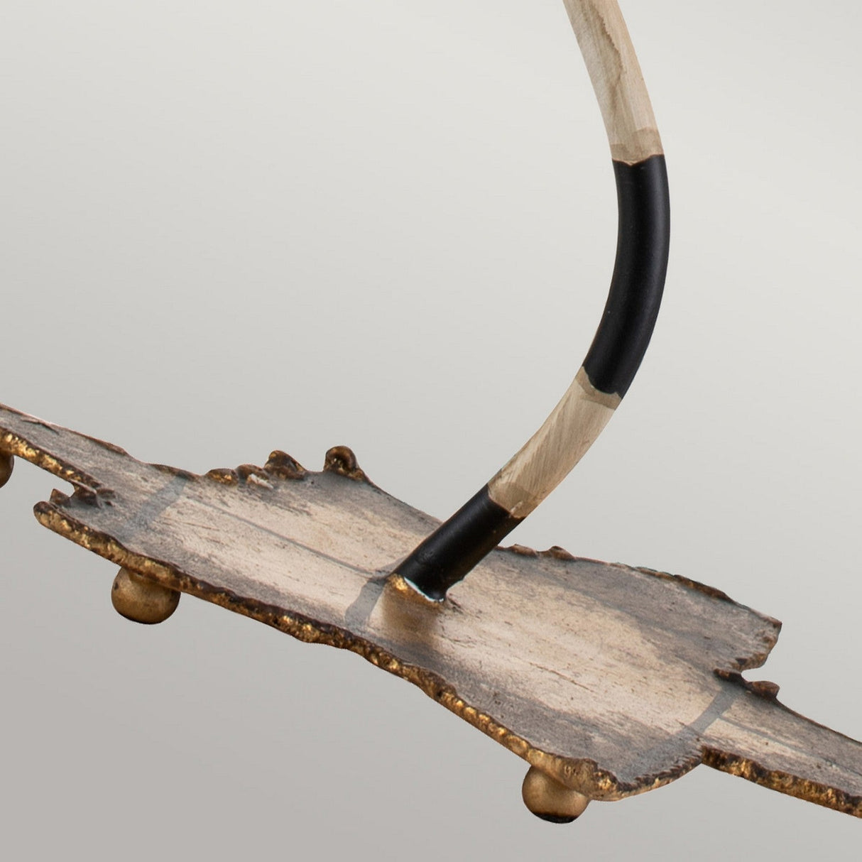 A close-up of the Dominique 1 Light Table Lamp showcases its modern, decorative metal sculpture design with an uneven, textured base. The lamp features a curved rod adorned in black and cream stripes extending upwards, while the base is highlighted by a rustic gold leaf finish against a plain light gray background.