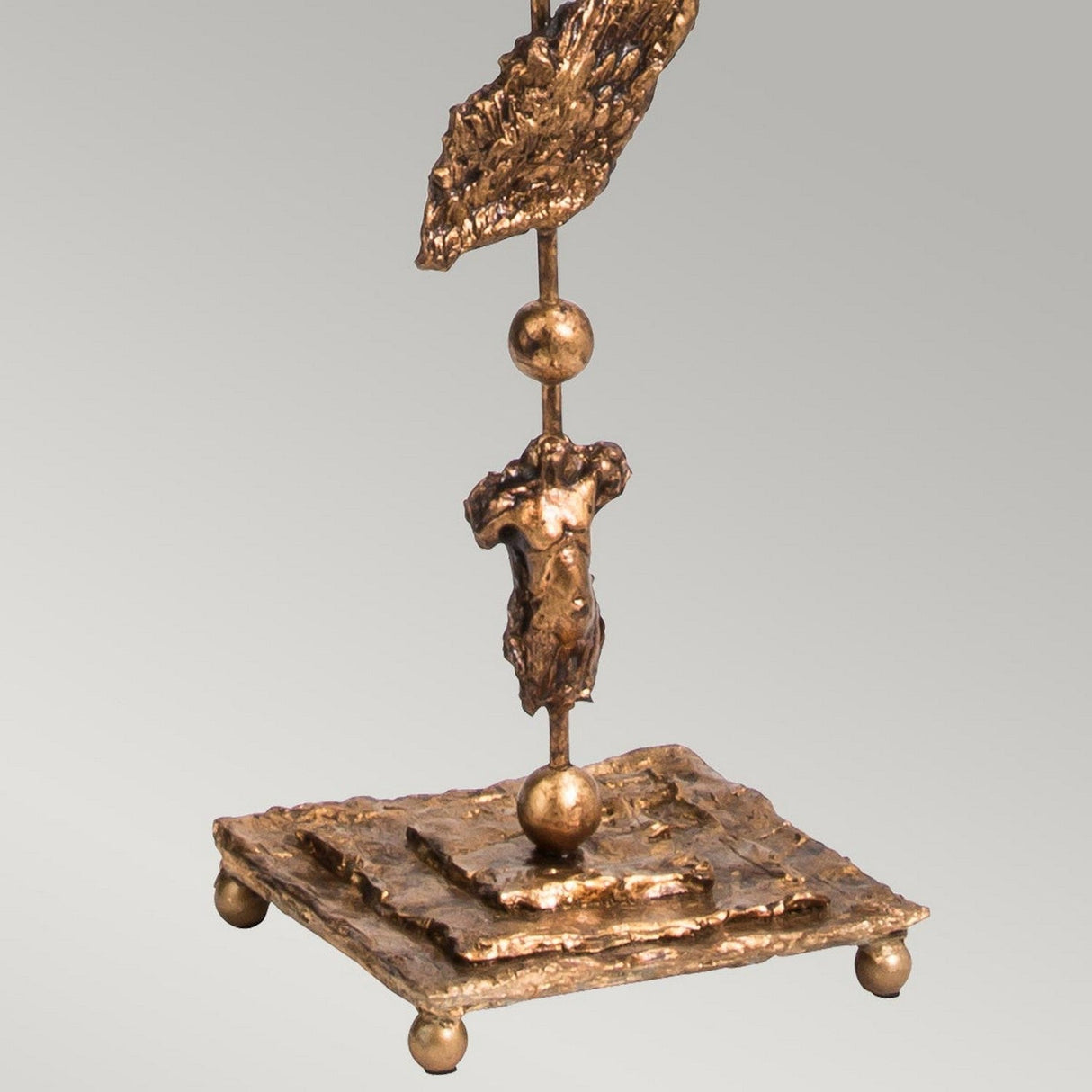 The Fragment 1 Light Floor Lamp in Aged Gold is a stunning piece featuring a bronze abstract sculpture with an aged gold finish. It boasts a textured base supporting a sphere, with a fragmented human figure rising towards another sphere and topped by an irregular, wing-like shape. This intriguing lamp comes alive under ambient lighting.