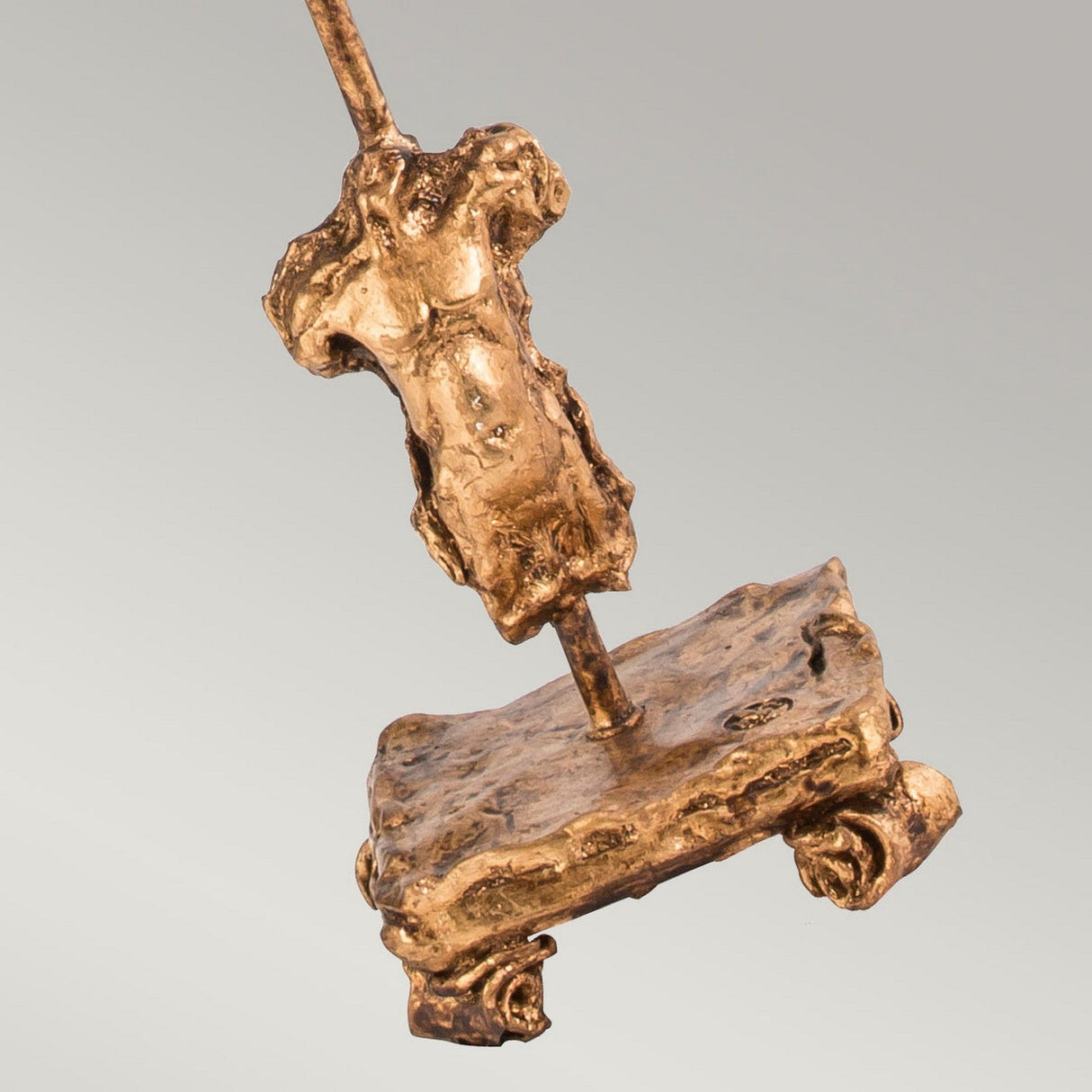 The Fragment 1 Light Table Lamp - Aged Gold showcases a textured bronze sculpture of an abstract human form on a rectangular base, smoothly integrated by a vertical rod. Its aged gold finish, with a rough patina, adds vintage charm while preserving a minimalist and modern design against a neutral backdrop.