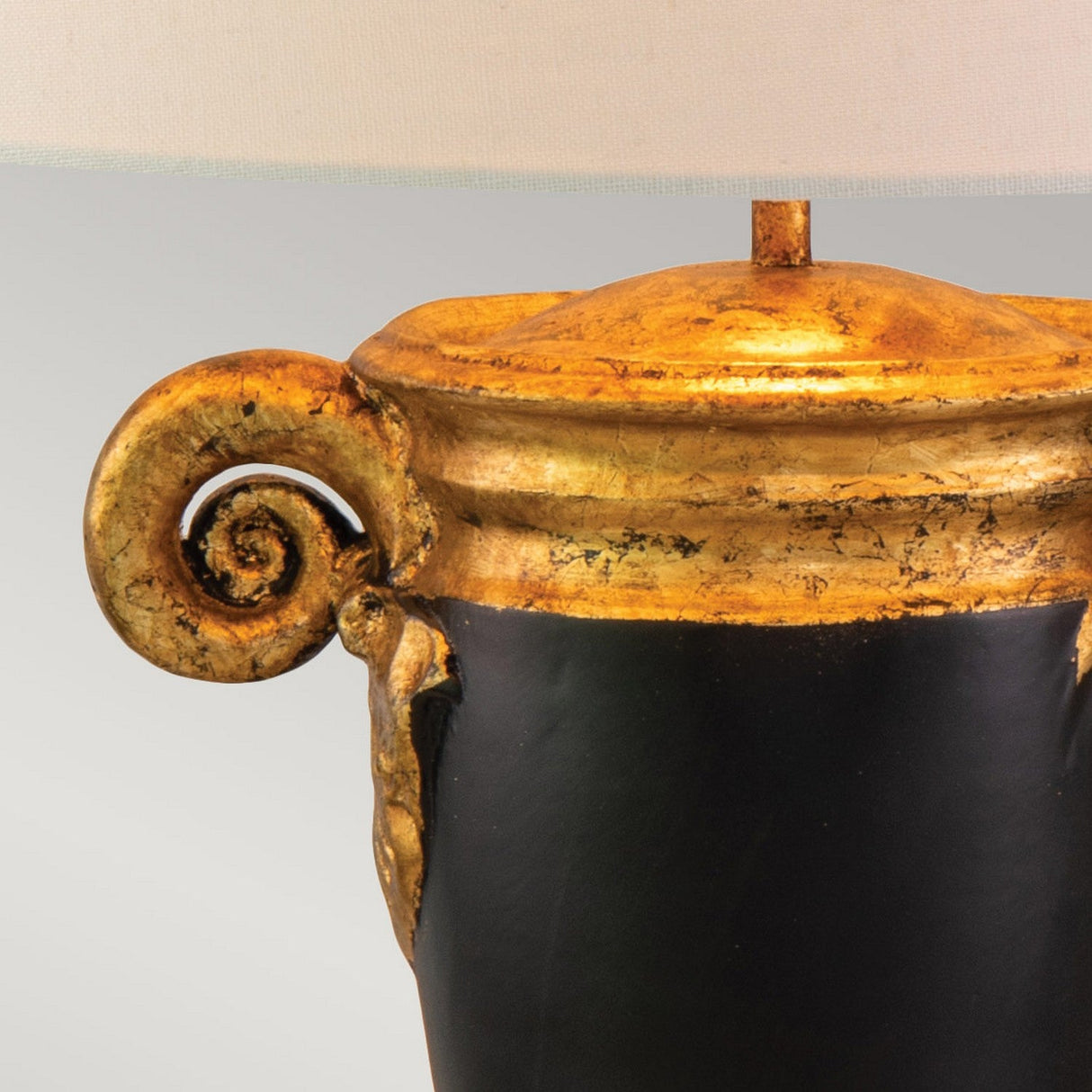 The Gallier 1 Light Table Lamp—Black & Gold—features an intricately designed base with a metallic gold finish and ram horn detailing, creating a striking contrast against its sleek black surface. This elegant piece of home decor is completed with a neutral shade, beautifully complementing the sophisticated black and gold color scheme against a plain backdrop.